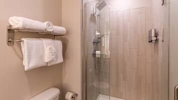 A modern bathroom with a glass-enclosed shower, a toilet, and a towel rack with neatly folded towels.
