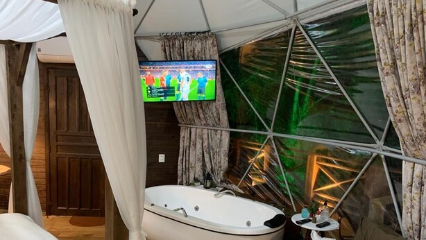 Ein Zimmer mit einer großen Badewanne, einem an der Wand montierten Fernseher und einem Vorhang.