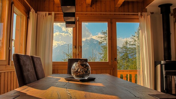 A wooden dining table with a glass bowl containing wood shavings, a laptop, and a chair.