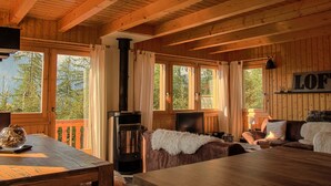 A cozy cabin interior with a fireplace, wooden furniture, and large windows offering a view of trees.