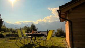 A wooden cabin with a table and chairs set outdoors, overlooking a mountainous landscape.