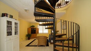 Un escalier en colimaçon avec des marches en bois et des rampes noires, menant à l’étage supérieur.
