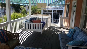 Une véranda couverte avec une balustrade blanche, un banc rembourré et un canapé avec des coussins à rayures.