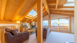 Een gezellige woonkamer met houten plafond, open haard en een bank.