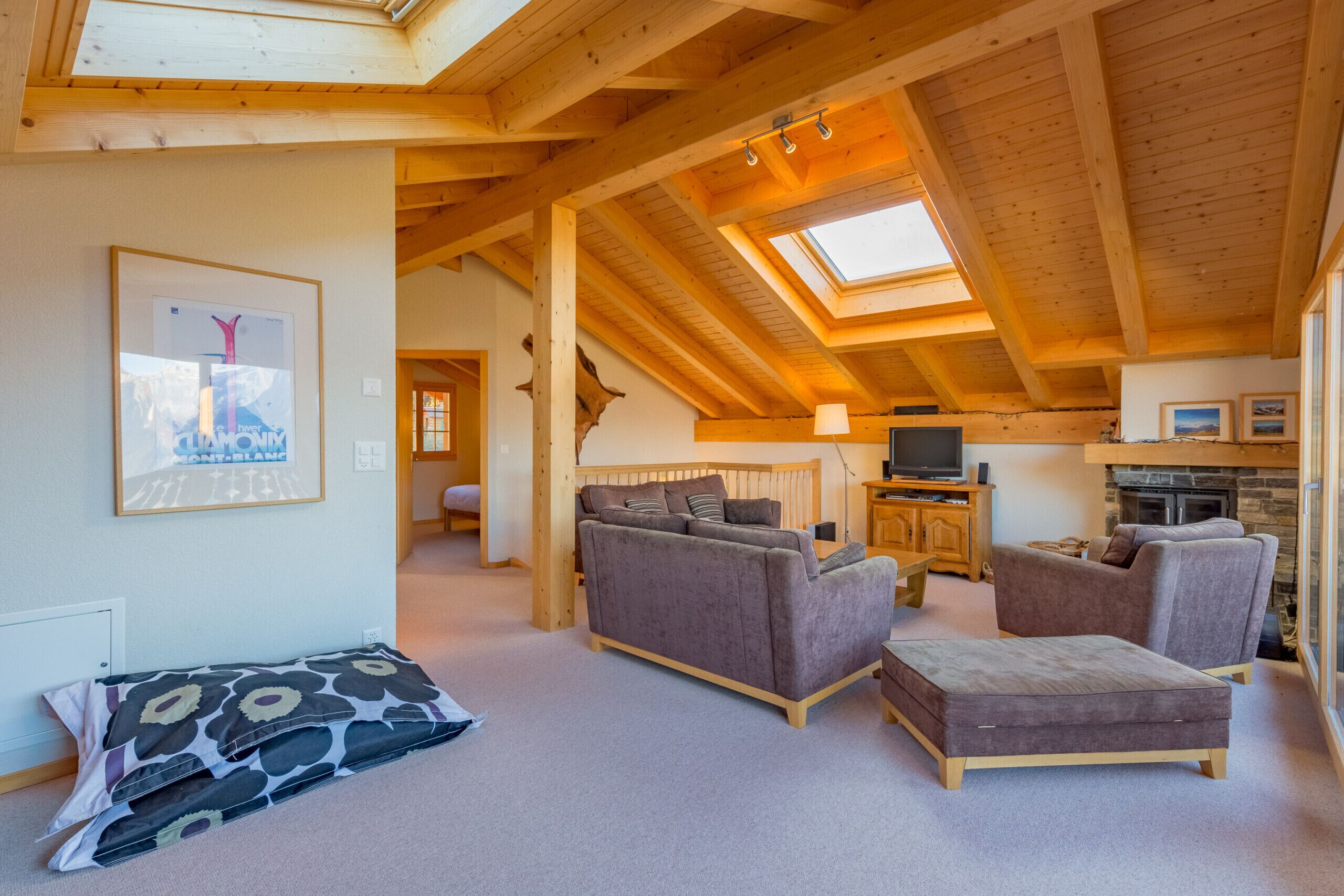 Een gezellige woonkamer met een hoge plafond, houten balken, een bank, een tweepersoonsbank, een televisie en een open haard.