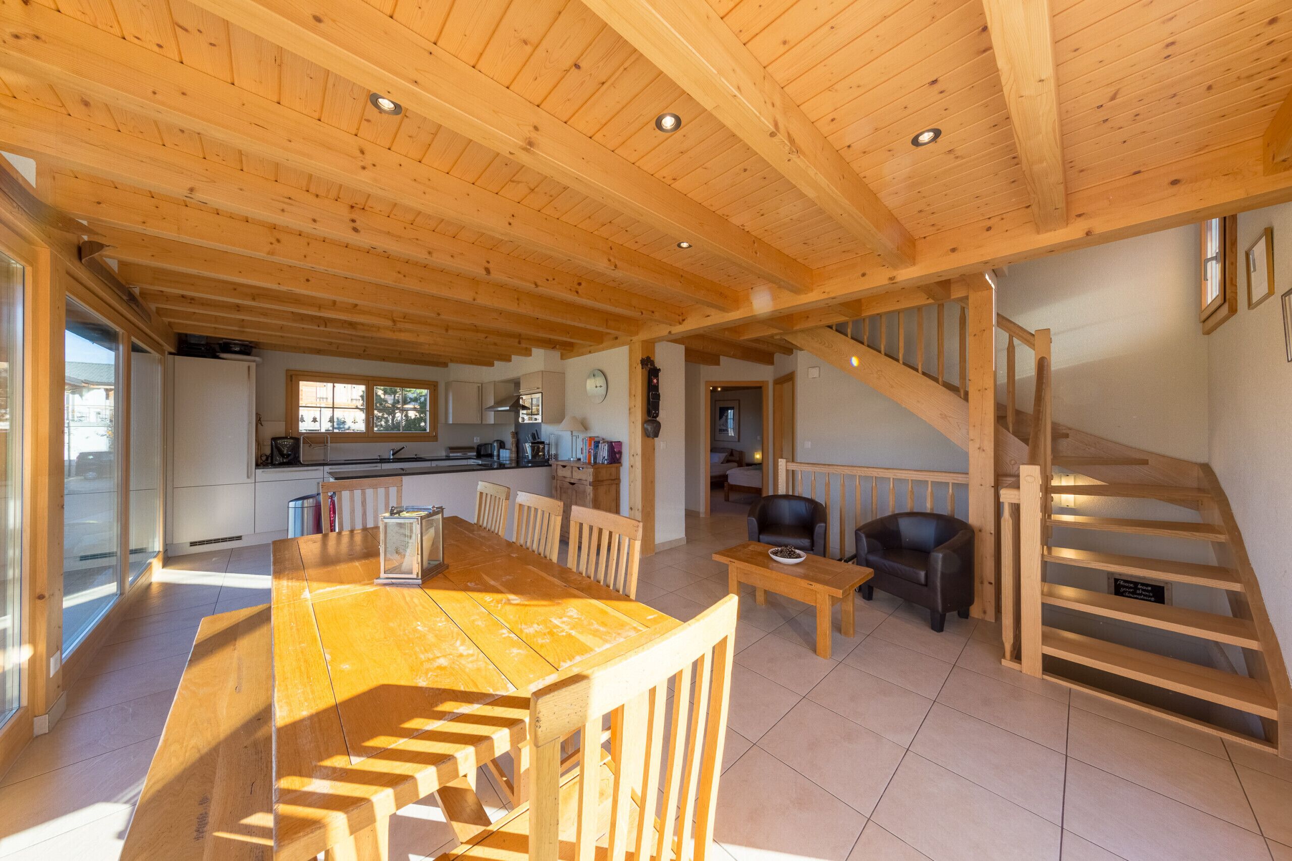 Un'ampia zona giorno con un tavolo da pranzo in legno e sedie, una scala e una cucina sullo sfondo.