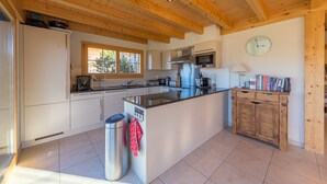 Een moderne keuken met houten balken, een centraal kookeiland, witte kasten, een roestvrijstalen prullenbak en een klok aan de muur.