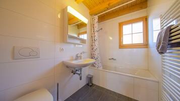Een moderne badkamer met een witte wastafel, een toilet, een bad en een douchegordijn.