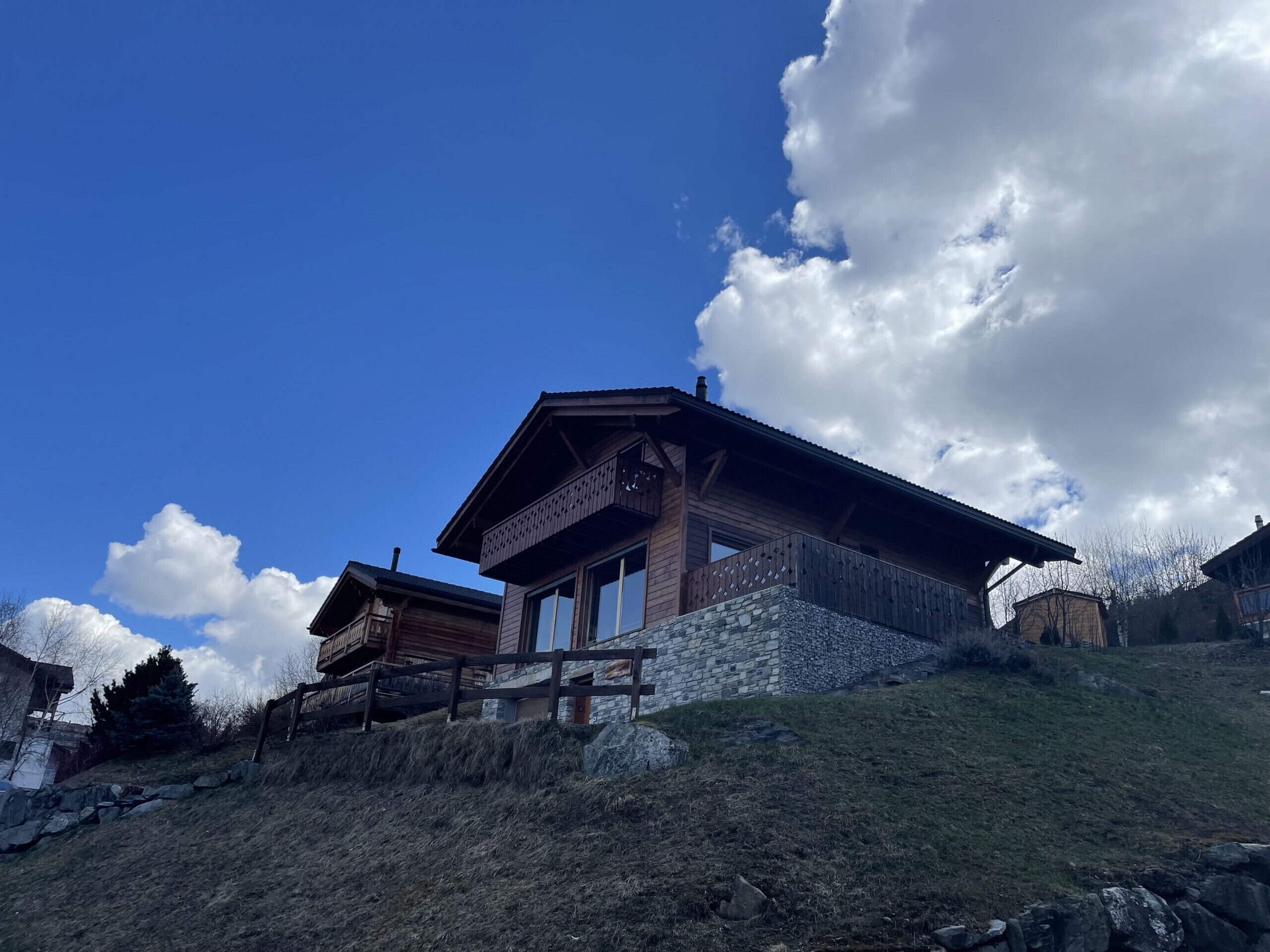 Een houten chalet met een stenen fundering, een balkon en uitzicht op het omliggende landschap.