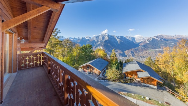 Een houten balkon met uitzicht op een bergketen en twee berghutten.