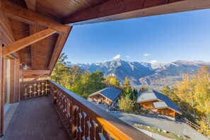 Een houten balkon met uitzicht op een bergketen en twee berghutten.