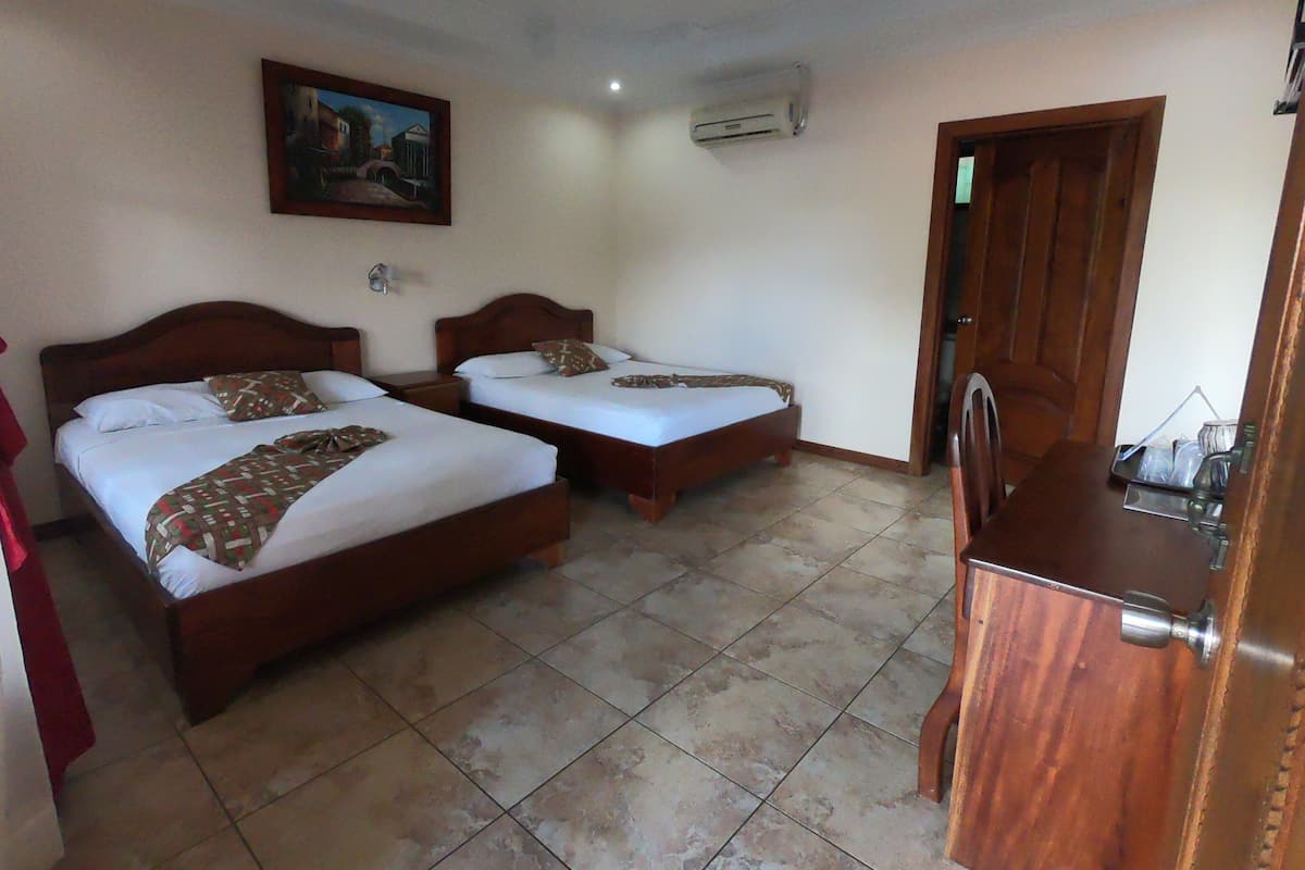 Een hotelkamer met twee houten bedden, een schilderij aan de muur, een airconditioner en een houten deur.