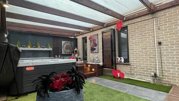 Un espace cuisine extérieur moderne, doté d’un barbecue, d’un jacuzzi et d’un mur décoratif orné d’une enseigne « Nid Angé ».