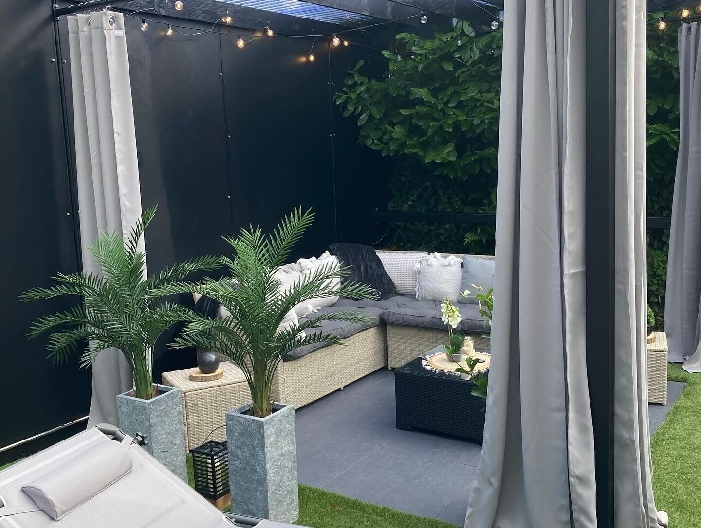 A covered outdoor seating area with a sofa, cushions, and potted plants.