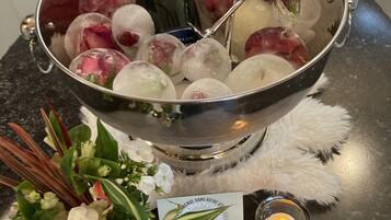 Een champagnefles in een metalen emmer met ijs en een glas, omringd door bloemen en een kaars op een tafel.