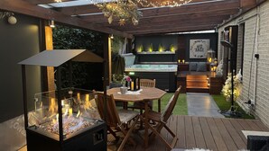 A cozy outdoor patio with a glass-enclosed fire feature, wooden furniture, and string lights. - Luxury gîte and spa in a romantic atmosphere for 2 people Max (Ohey)