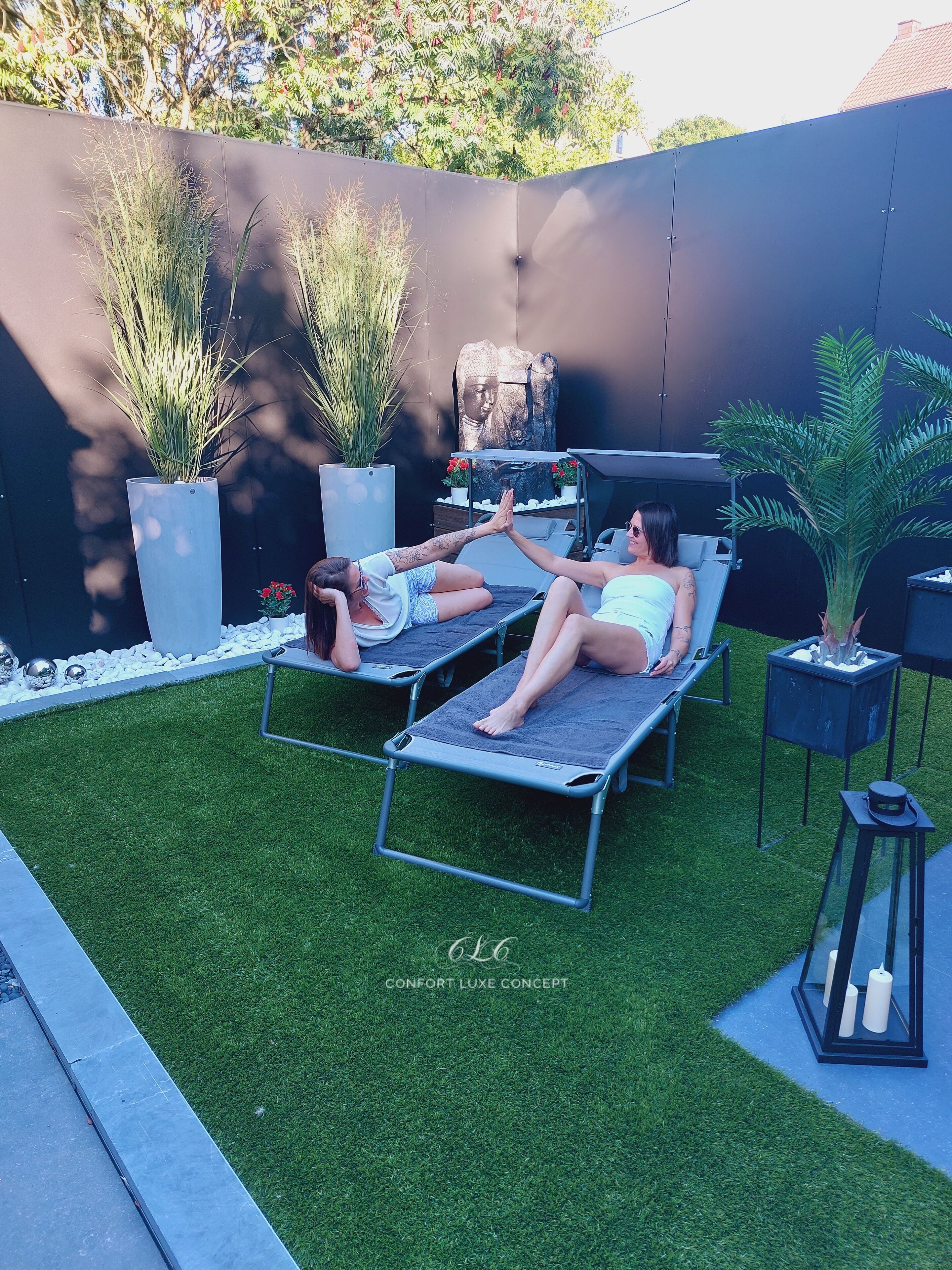 Two lounge chairs on artificial grass with a modern outdoor kitchen and potted plants in the background.