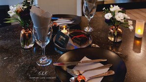 A dining area with a table set for two, a TV displaying a fire scene, and a mirror reflecting the room. - Luxury gîte and spa in a romantic atmosphere for 2 people Max (Ohey)