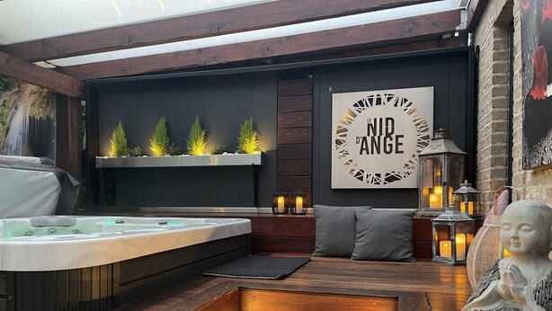 A modern outdoor hot tub area with wooden steps, a seating area, and a wall-mounted shelf with plants. - Luxury gîte and spa in a romantic atmosphere for 2 people Max (Ohey)