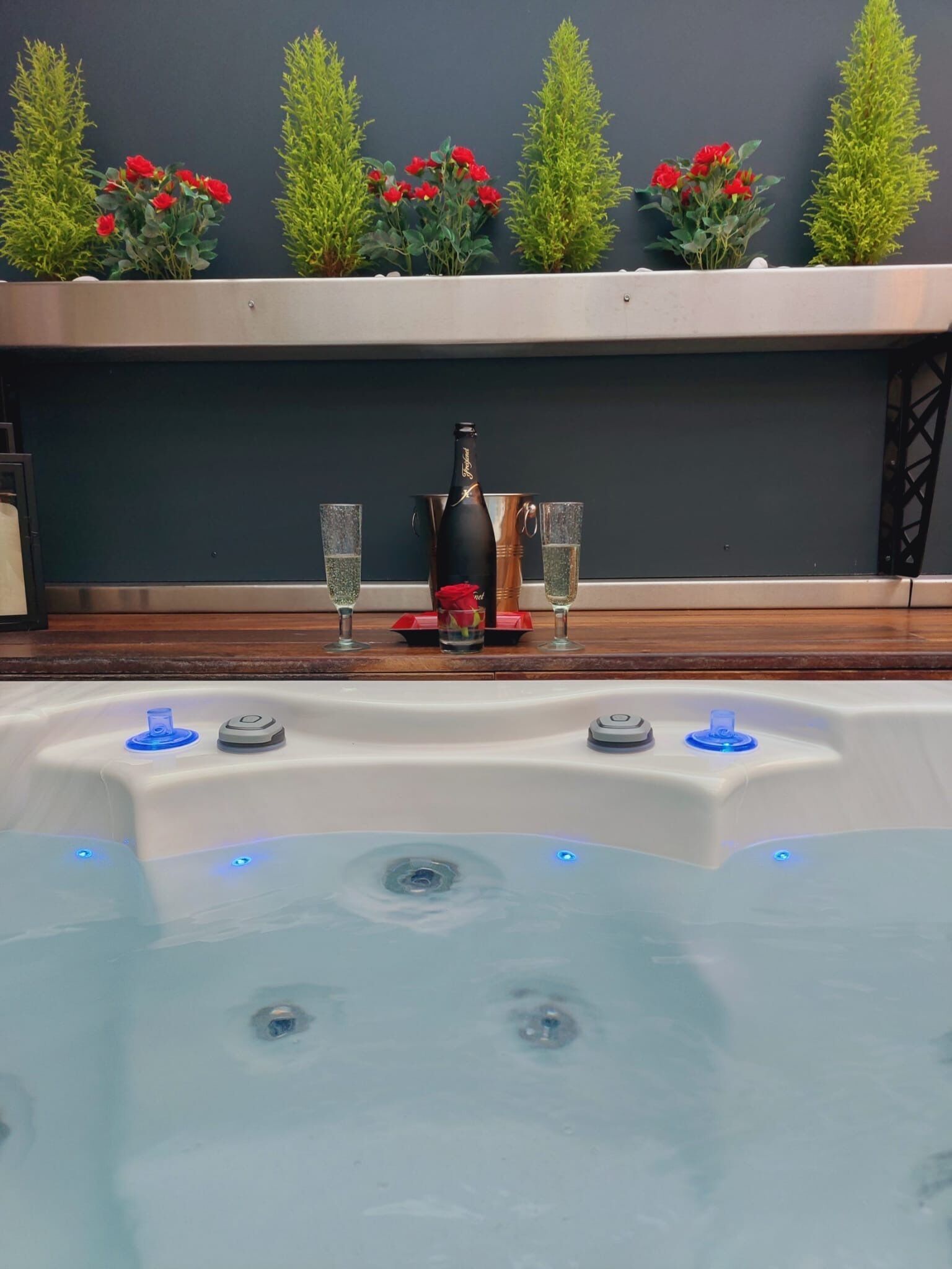 Un jacuzzi con chorros, una botella de champán y dos copas sobre una terraza de madera.