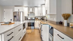 A modern kitchen with white cabinets, stainless steel appliances, and a wooden countertop.