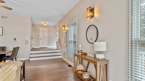 A modern interior with a staircase leading to another level, a dining area with a table and chairs, and a console table with a lamp and decorative items.