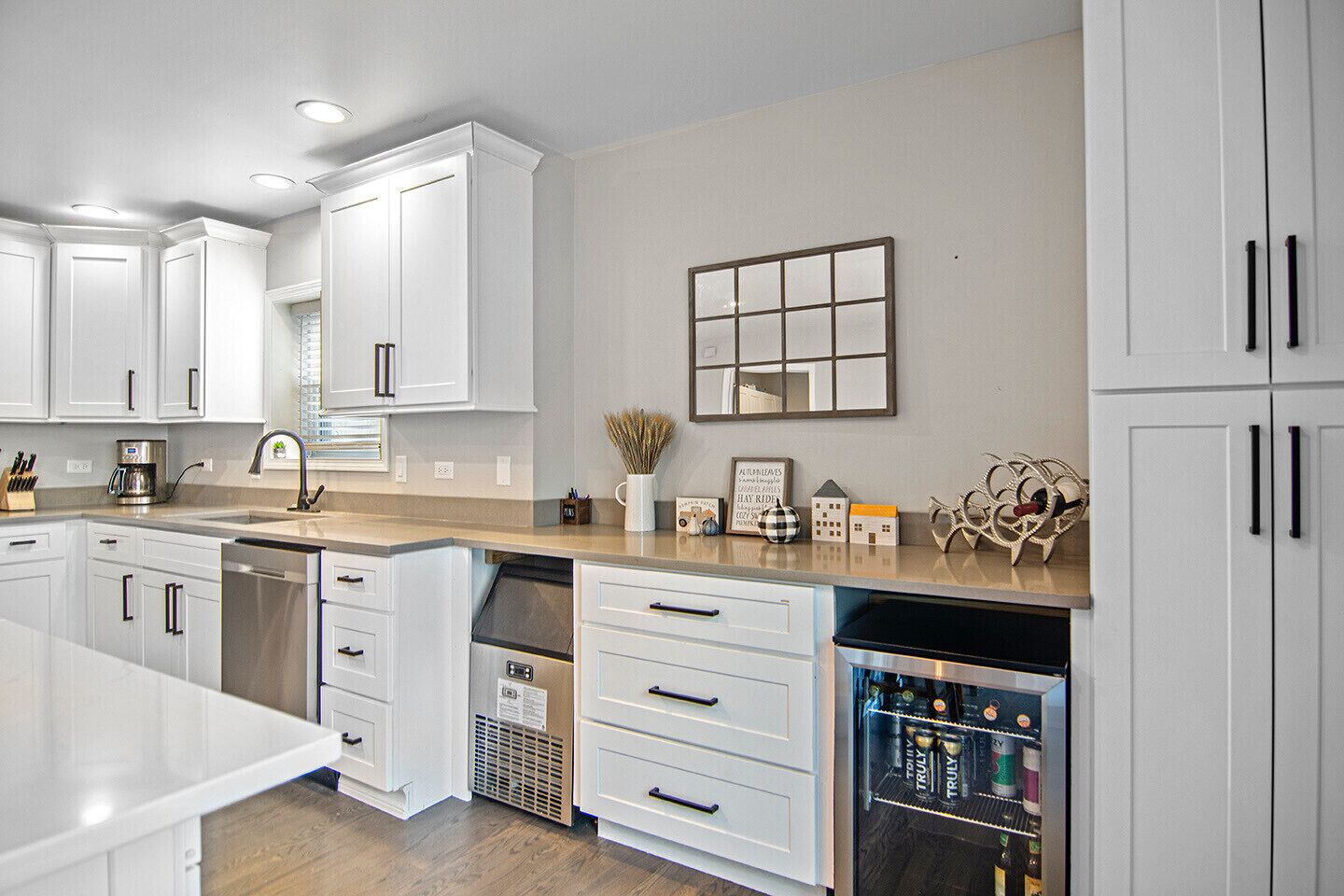 A modern kitchen with white cabinetry, a built-in dishwasher, and a countertop with a coffee maker and decorative items.