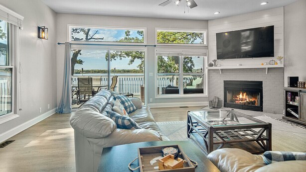 A spacious living room with a fireplace, large windows, and a balcony.
