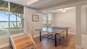 A spacious room with a ping pong table, large windows, and a staircase leading to an outdoor area.