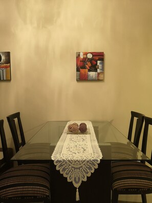 A dining table with a glass top, surrounded by chairs, and a lace table runner. - Quantum Park (Asunción)