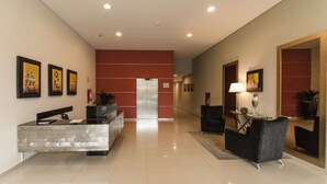 A modern lobby with a reception desk, a waiting area with chairs, and a large mirror. - Quantum Park (Asunción)
