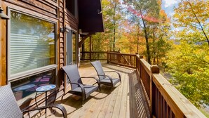 A wooden deck with two chairs and a table, overlooking a forest with autumn foliage. - High Country Home (McHenry)