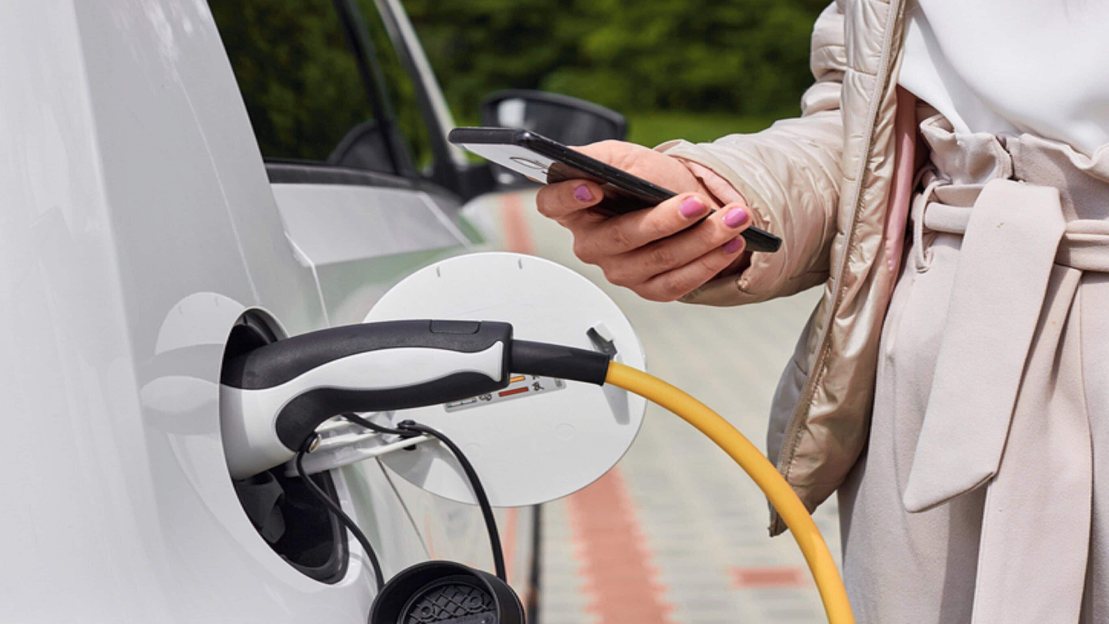 A person charging an electric vehicle with a yellow cable.