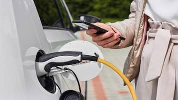 A person charging an electric vehicle with a yellow cable.