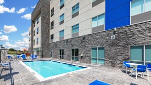 Un hôtel moderne doté d’une piscine, de chaises longues bleues et d’une façade en pierre.