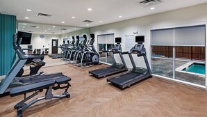 Un centre de remise en forme équipé de tapis de course, d’un appareil d’aviron et d’un espace piscine visible à travers de grandes fenêtres.