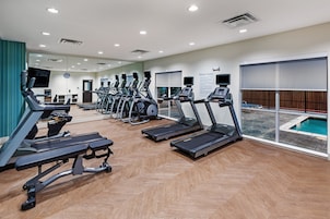A fitness center with treadmills, a rowing machine, and a pool area visible through large windows.