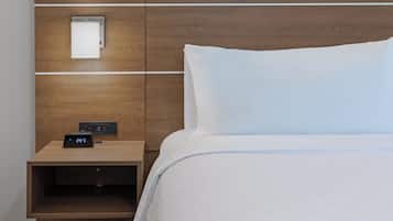 Habitación de hotel con una cama, una mesita de noche con un reloj digital y un enchufe.