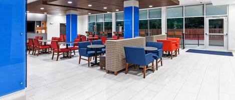 A modern indoor seating area with red and blue chairs, a patterned wall, and large windows.