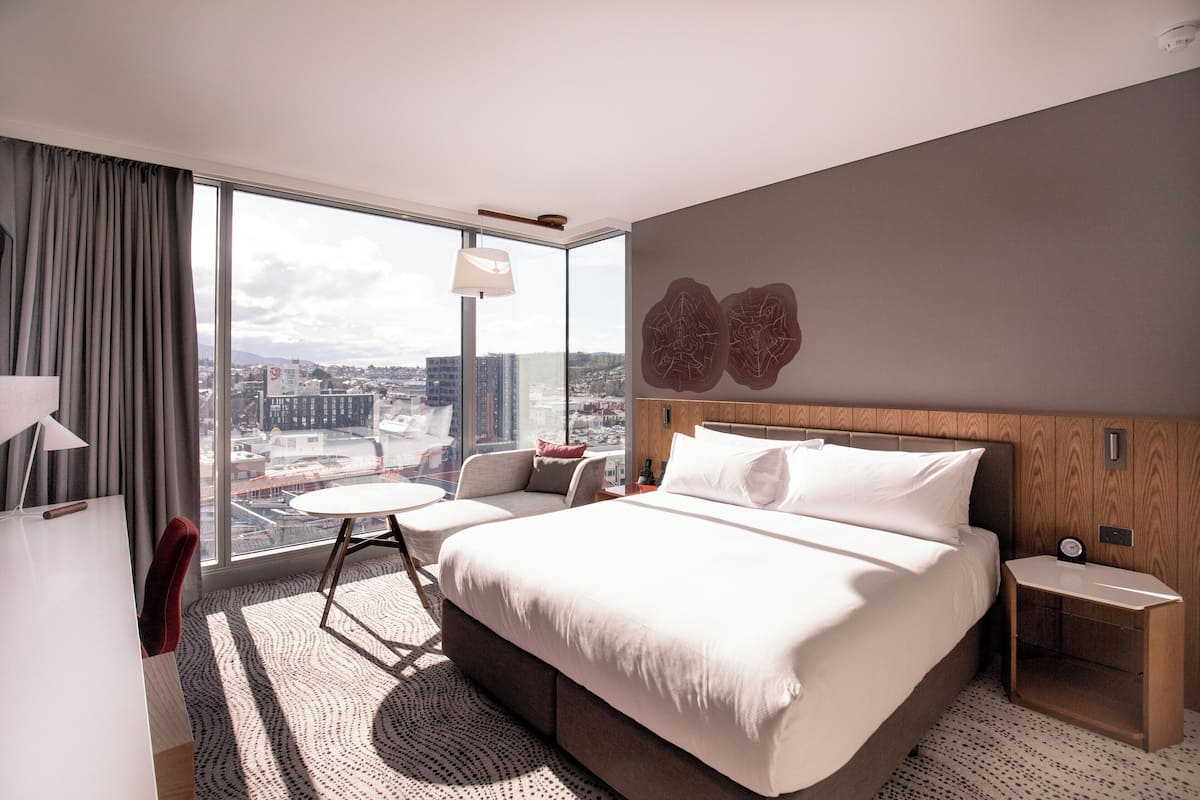 Een moderne hotelkamer met een groot bed, een bureau, een stoel en uitzicht op de stad.