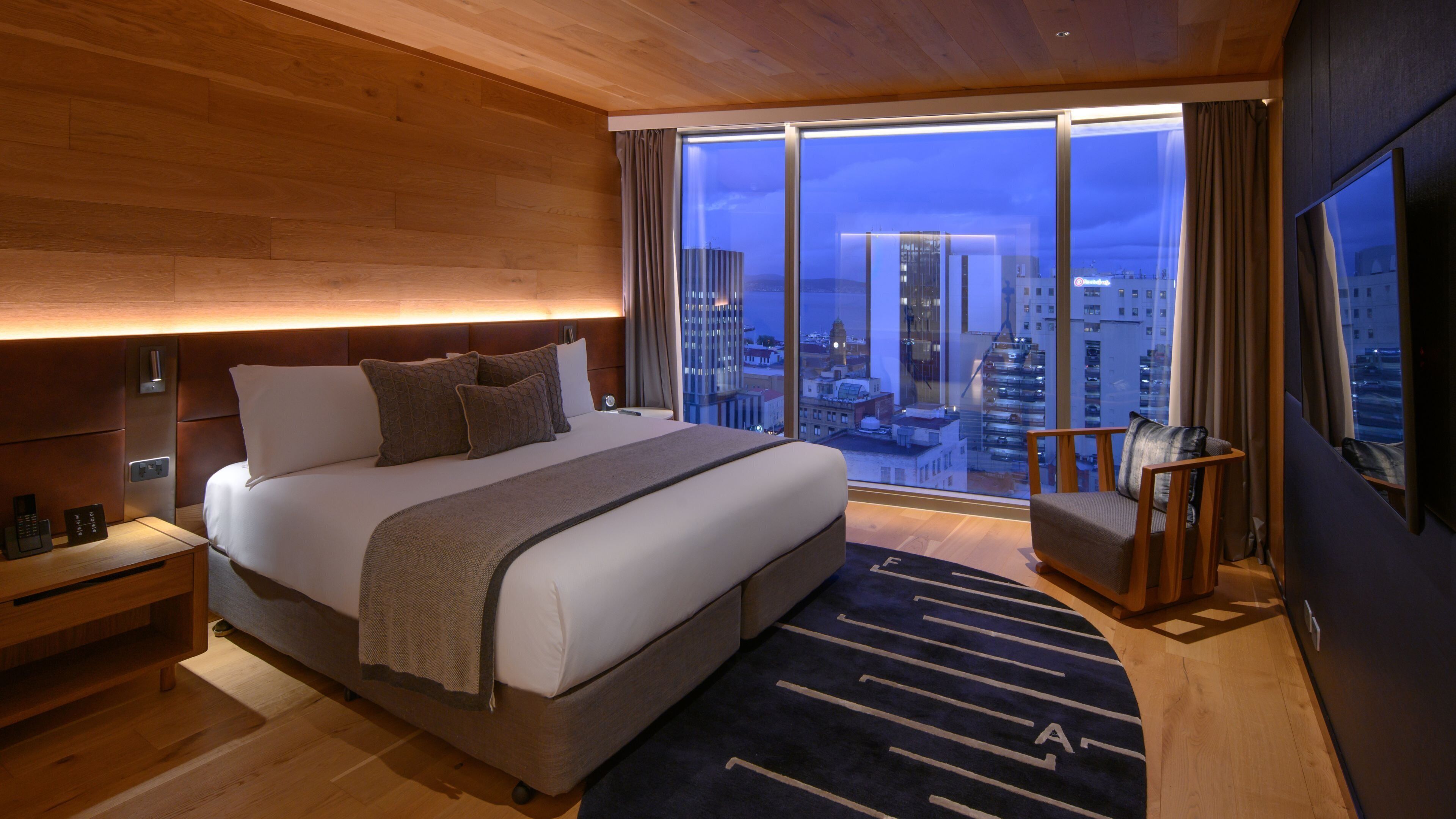 A modern hotel room with a large bed, a seating area, and a city view.