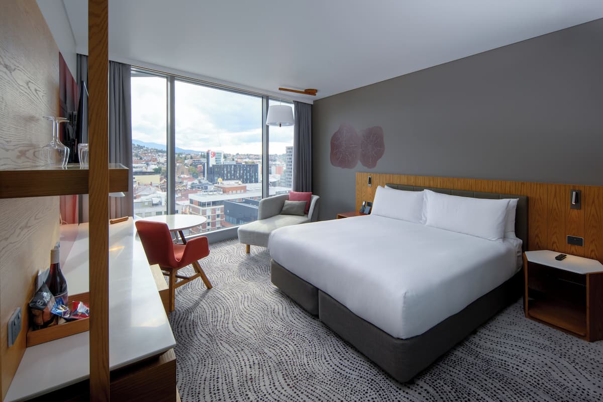 Een hotelkamer met een groot bed, een bureau, een stoel en uitzicht op de stad.