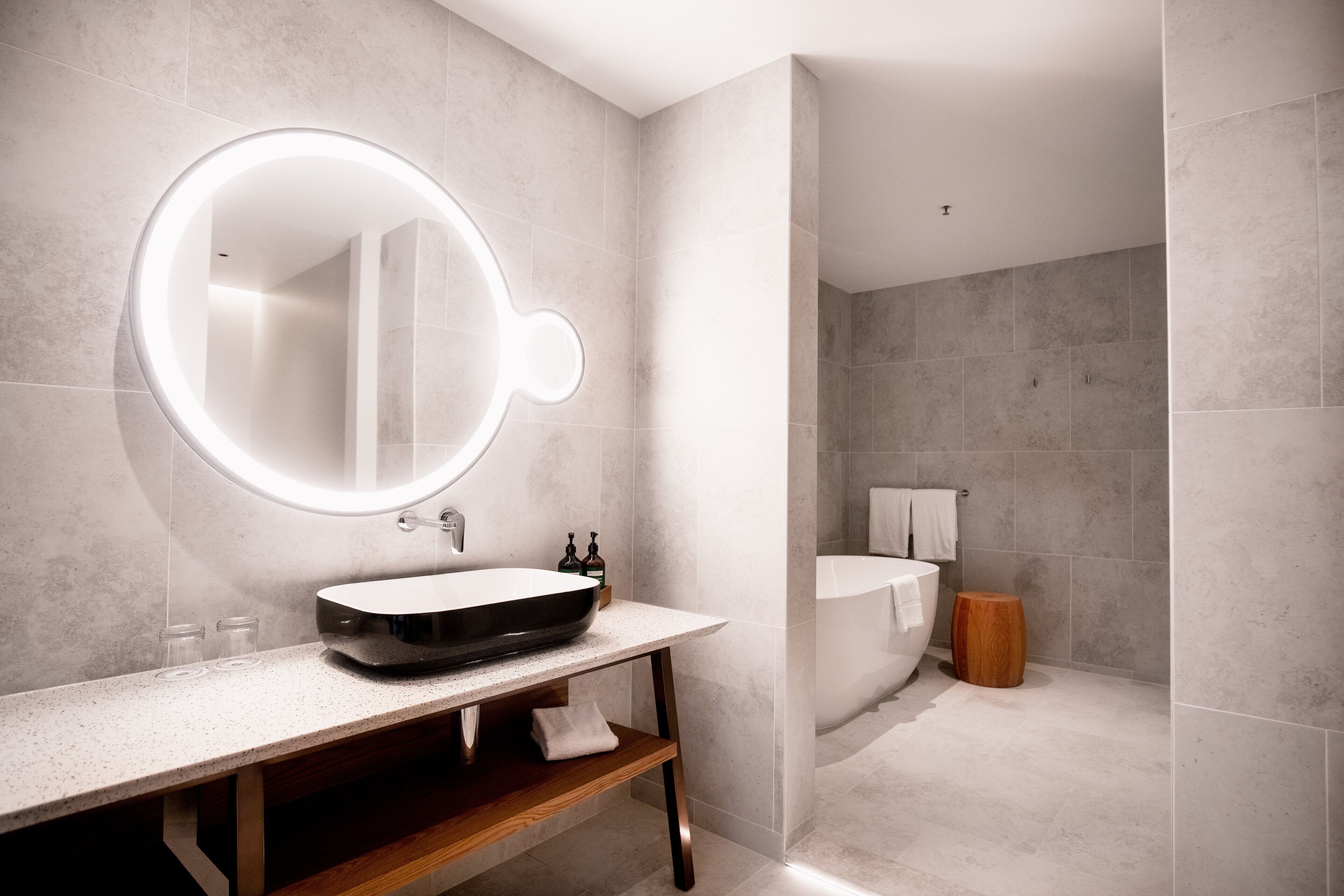 Un baño moderno con un espejo redondo, un lavamanos independiente y una zona de ducha separada.