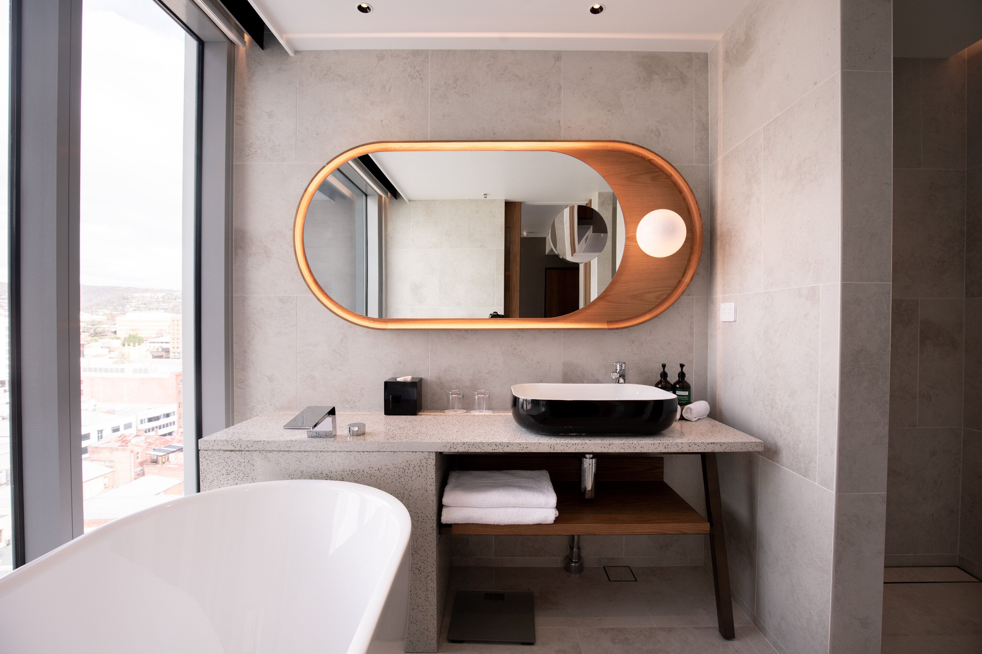 A modern bathroom with a freestanding bathtub, a large mirror with a wooden frame, a sink with a black basin, and a towel rack.