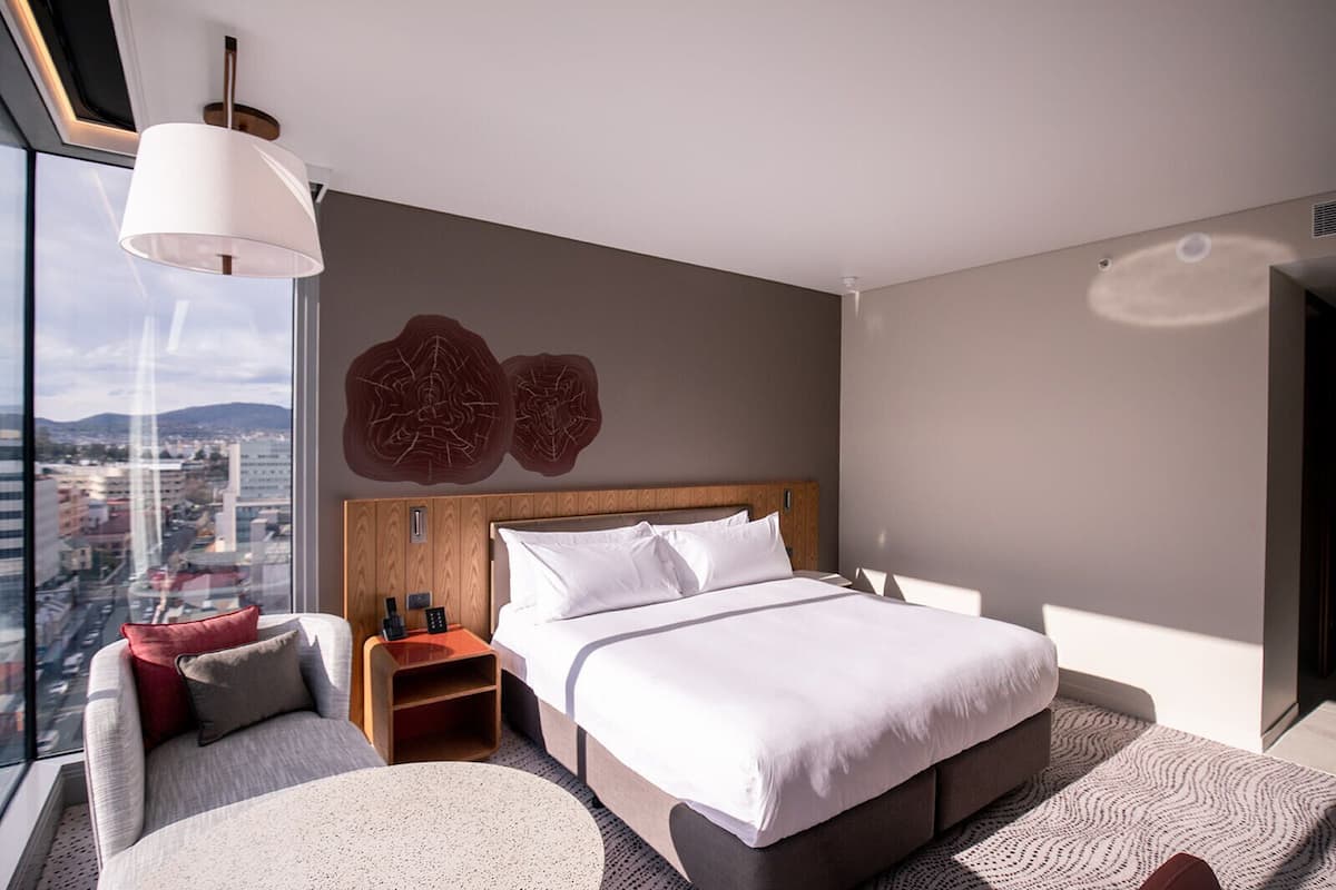 Een moderne hotelkamer met een groot bed, nachtkastje, stoel en uitzicht op de stad.