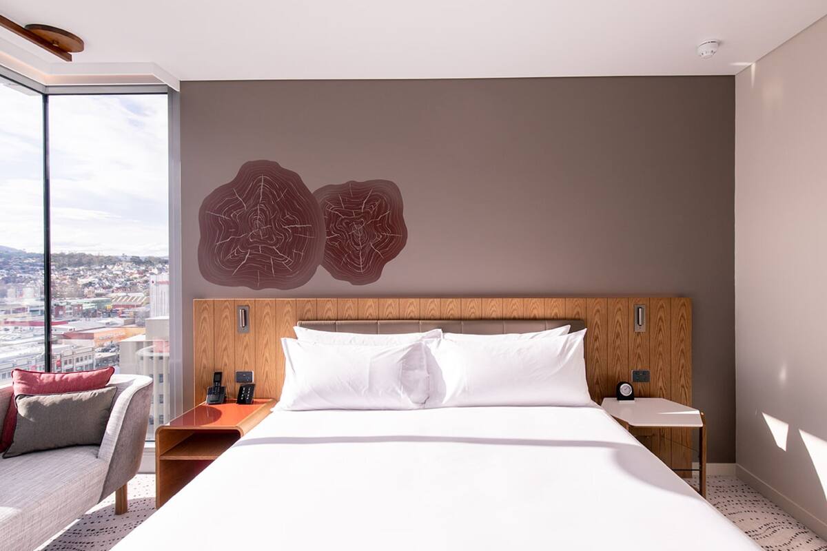 Une chambre d’hôtel moderne dotée d’un grand lit, d’une tête de lit en bois, d’une vue sur la ville et d’un mur en verre.