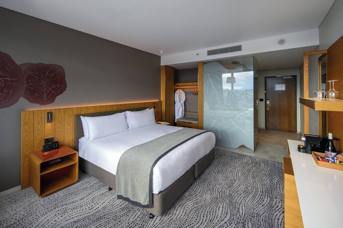 Une chambre d’hôtel moderne avec un grand lit, une table de chevet en bois, un bureau avec une chaise, un peignoir et un miroir.
