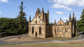 A historic stone building with multiple pointed towers and arched windows, surrounded by a grassy area and trees.