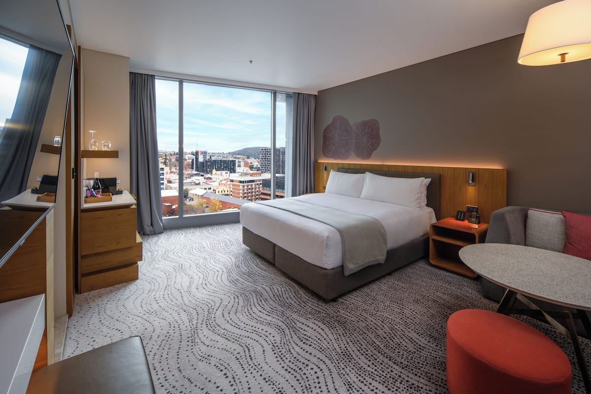 Een hotelkamer met een groot bed, een bureau, een stoel, een kleine tafel en uitzicht op de stad.