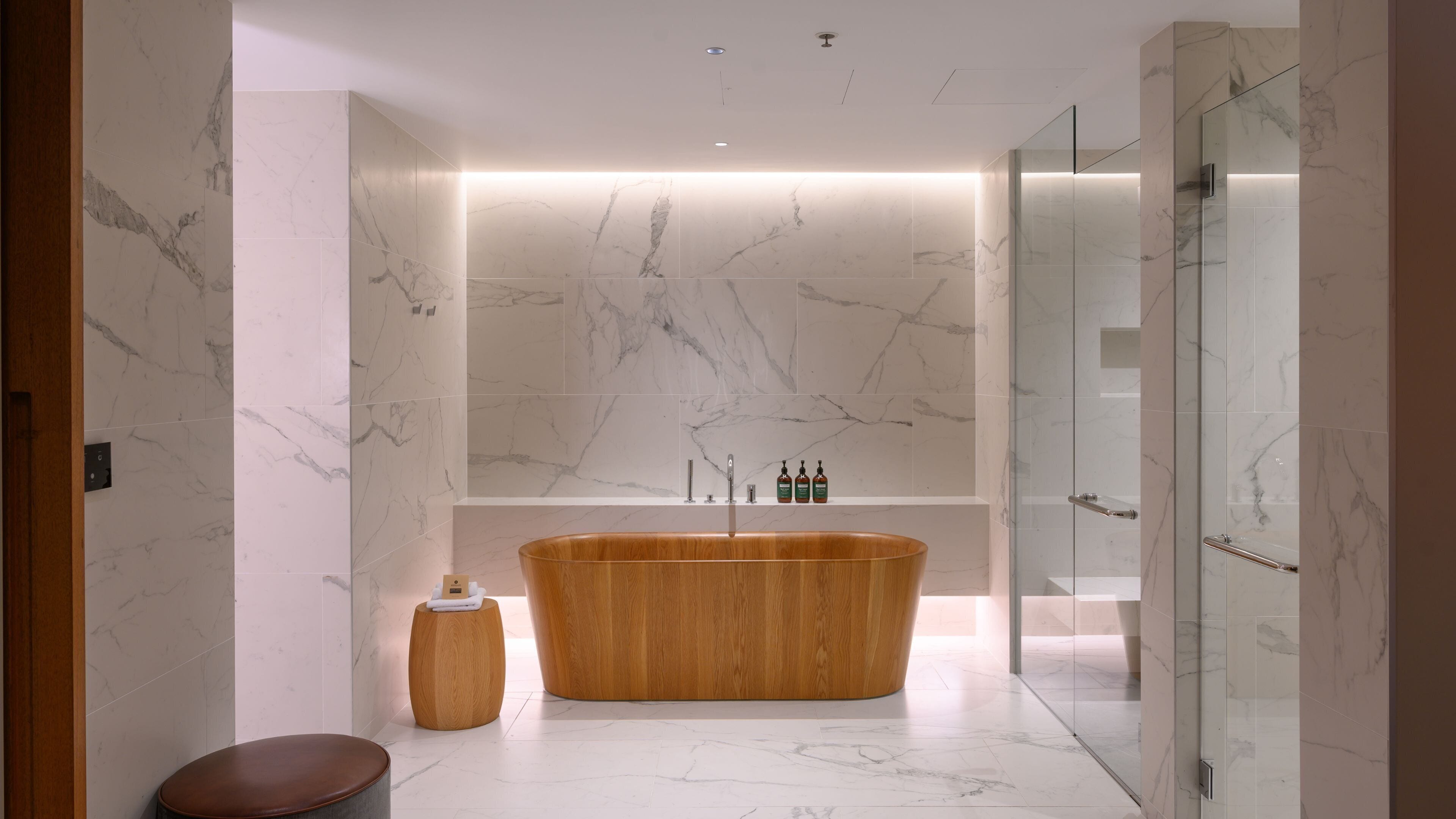 A modern bathroom with a freestanding bathtub, a glass shower enclosure, and a marble-tiled wall.